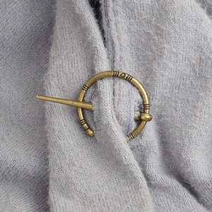 Gros plan d'une broche Viking en bronze de style vintage sur un gilet en maille mauve