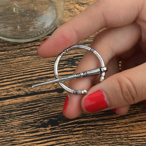 Détail d'une broche Viking vintage en alliage argenté sur fond bois tenu à la main