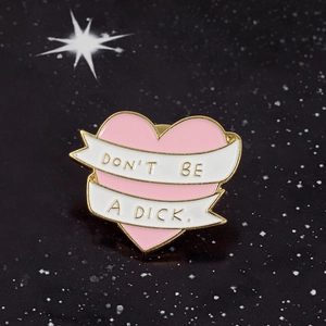 Pink heart enamel pin with Don't Be A Dick slogan on golden metal badge background