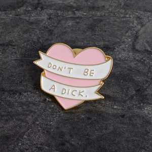 Pink heart enamel pin with Don't Be A Dick ribbon motif and golden alloy plating