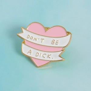 Pink heart enamel pin with gold metal edges and Don’t Be A Dick white ribbon text