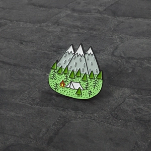 Outdoor adventure enamel pin featuring snow mountains, forest, tent, and campfire design