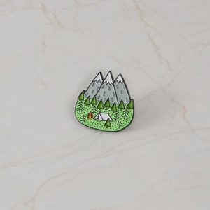 Outdoor adventure enamel pin featuring snow mountains, forest, tent, and campfire