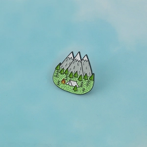 Outdoor camping enamel pin featuring snow-capped peaks, pine forest, and a cozy campfire