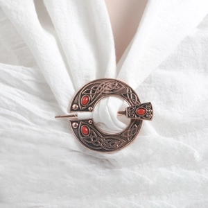 Detailed macro view of Celtic knot brooch with red cabochons on white fabric texture