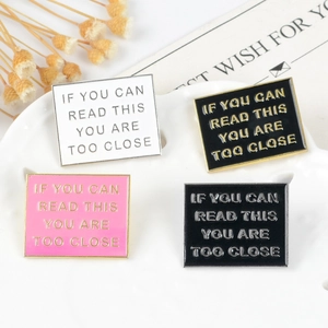 Set of four square enamel warning pins in various colors on a white ceramic tray