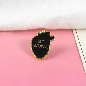 Gros plan détaillé du pin's cœur en émail avec inscription Be Brave et bords dorés