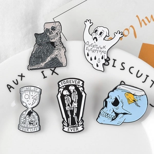 Gothic enamel pin set with skull, ghost, and hourglass motifs displayed on a white plate