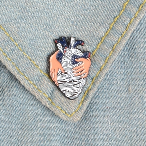 Spilla cuore anatomico con cavo USB e mani avvolgenti su sfondo in tessuto denim