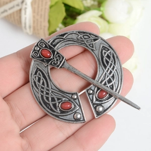 Detail of vintage Celtic knot brooch with red gemstones held in hand for size reference