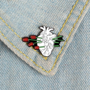Artistic anatomical heart enamel brooch with red tulips pinned on blue denim fabric