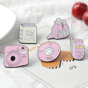 Detailed set of five pink enamel pins featuring a backpack, camera, and cute cartoon designs