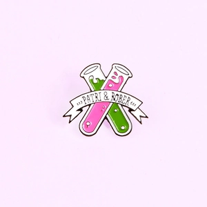 Detail view of enamel test tube brooch with green pink liquid and ribbon inscription
