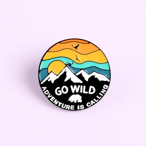 Detail of round enamel pin featuring snowy mountains, sunset and Go Wild adventure text