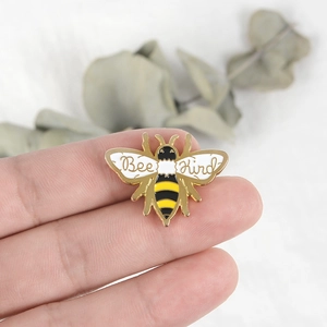 Handheld photo of Bee Kind enamel brooch with yellow black stripes and gold plating