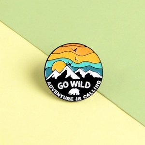 Close-up of enamel pin with sunset snowy mountains and Go Wild adventure text
