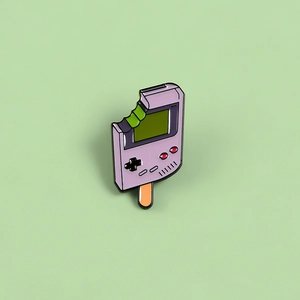 Macro shot of creative purple Game Boy popsicle enamel pin on soft green background