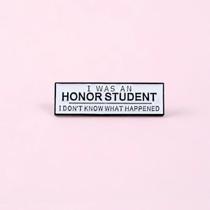 Detail of rectangular enamel pin featuring black text on white background with pink backdrop