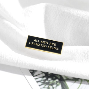Rectangular black enamel pin with gold text reading ALL MEN ARE CREMATED EQUAL