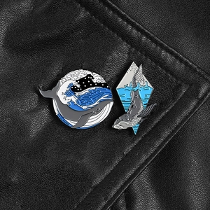 Detail of whale enamel pins with ocean wave designs pinned on a black leather collar