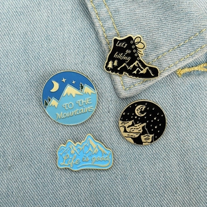Enamel pin set featuring mountain scenes and hiking shoes on blue denim background