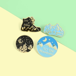 Close-up of four outdoor hiking enamel pins featuring mountain peaks and hiking boots