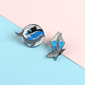 Detailed view of two ocean whale enamel pins featuring wave patterns on a pastel background