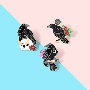 Close-up of three dark gothic crow enamel pins with skull, red rose and moon details