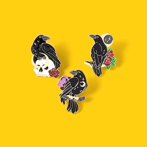 Gothic black raven skull and rose enamel pin set with gold trim on yellow background