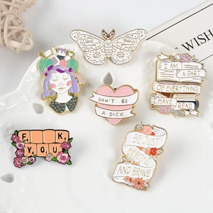 Detail shot of cartoon enamel pins with motivational quotes on a white ceramic tray