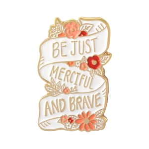 Detail of enamel pin with floral ribbon design and Be Just Merciful and Brave text