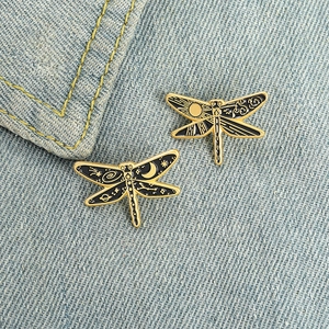 Creative dragonfly enamel pins with sun and moon celestial motifs on denim jacket