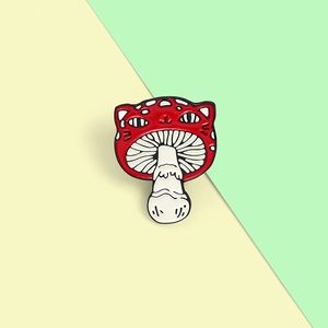 Gros plan sur une épingle en émail créative alliant champignon rouge et tête de chat