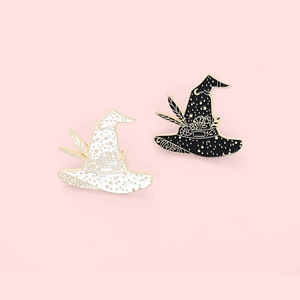 Dettaglio di spille smaltate a cappello di strega bianco e nero con fiori e luna crescente