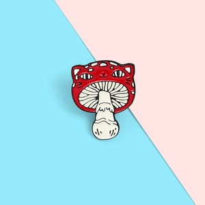 Detailed view of the cute red mushroom enamel pin with a cartoon cat face on pink background
