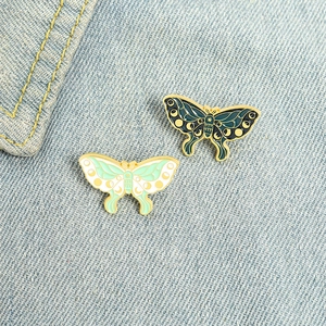Cartoon enamel butterfly pins set with moon phase patterns on blue denim background