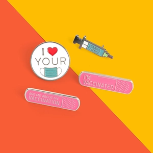 Close-up of four colorful medical enamel pins with vaccine themes on a dual-tone background