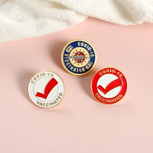 Macro shot of three COVID-19 vaccinated commemorative enamel pins on a pink surface