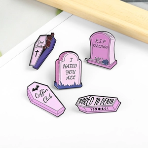 Flat lay of five pink and purple gothic coffin and tombstone enamel badges on white background