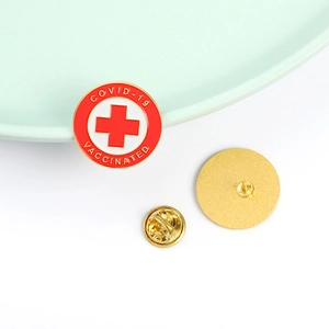 Macro shot of circular enamel medical brooch with red cross and vaccinated text