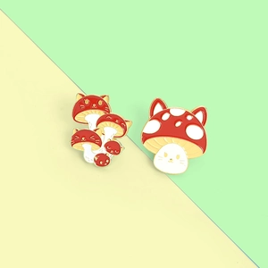 Detailed view of two cute cat-head mushroom enamel pins with red polka dot caps