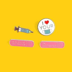 Medical enamel pin set with pink band-aid and blue syringe shapes on yellow background