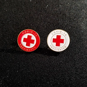 Detail of red and white circular enamel pins featuring COVID-19 VACCINATED text and crosses