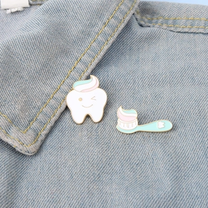 Cartoon enamel tooth and toothbrush brooch set pinned on light blue denim fabric background