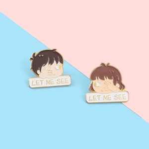 Detail view of cartoon couple enamel pins with 'LET ME SEE' text on split background