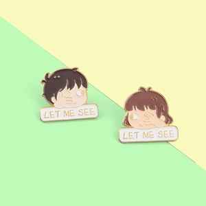 Detail view of cartoon enamel couple pins featuring a boy and girl with 'LET ME SEE' text