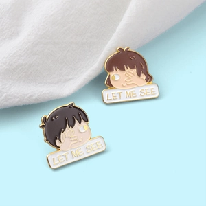 Detail of cartoon enamel pins with gold finish showing couples and Let Me See text
