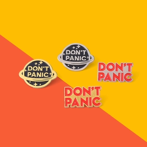 Macro detail of four 'DON'T PANIC' enamel pins in planet and text shapes with metal finish