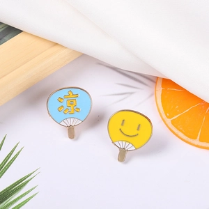 Détail de deux broches en émail en forme d'éventails japonais sur fond estival frais