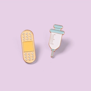 Detailed macro view of cartoon band-aid and syringe enamel pins with golden metal edges